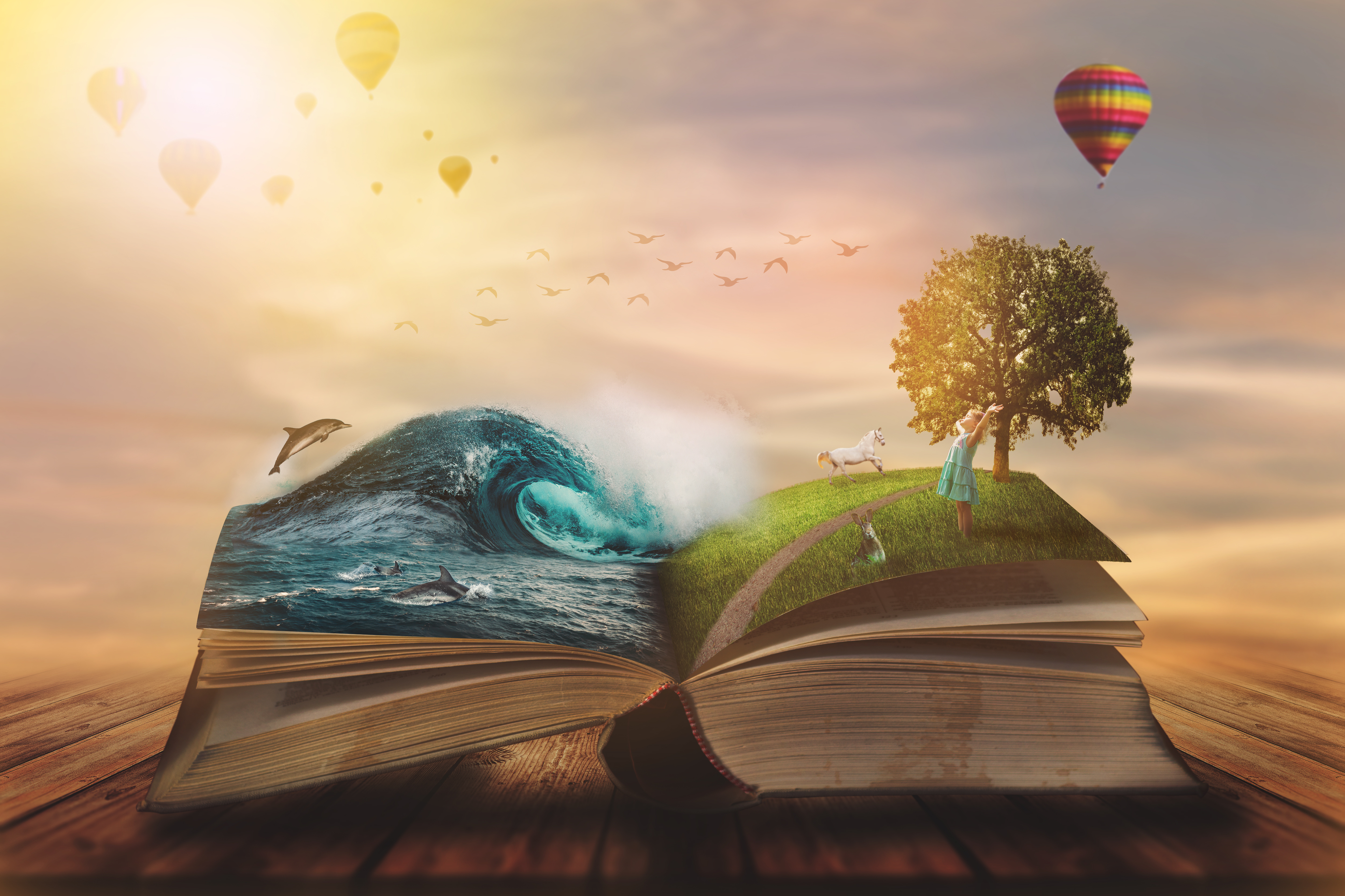 An open book on a wooden table with vibrant scenes emerging from its pages, including a wave with dolphins, a grassy hill with a girl and a unicorn, and hot air balloons in a dreamy sky.
