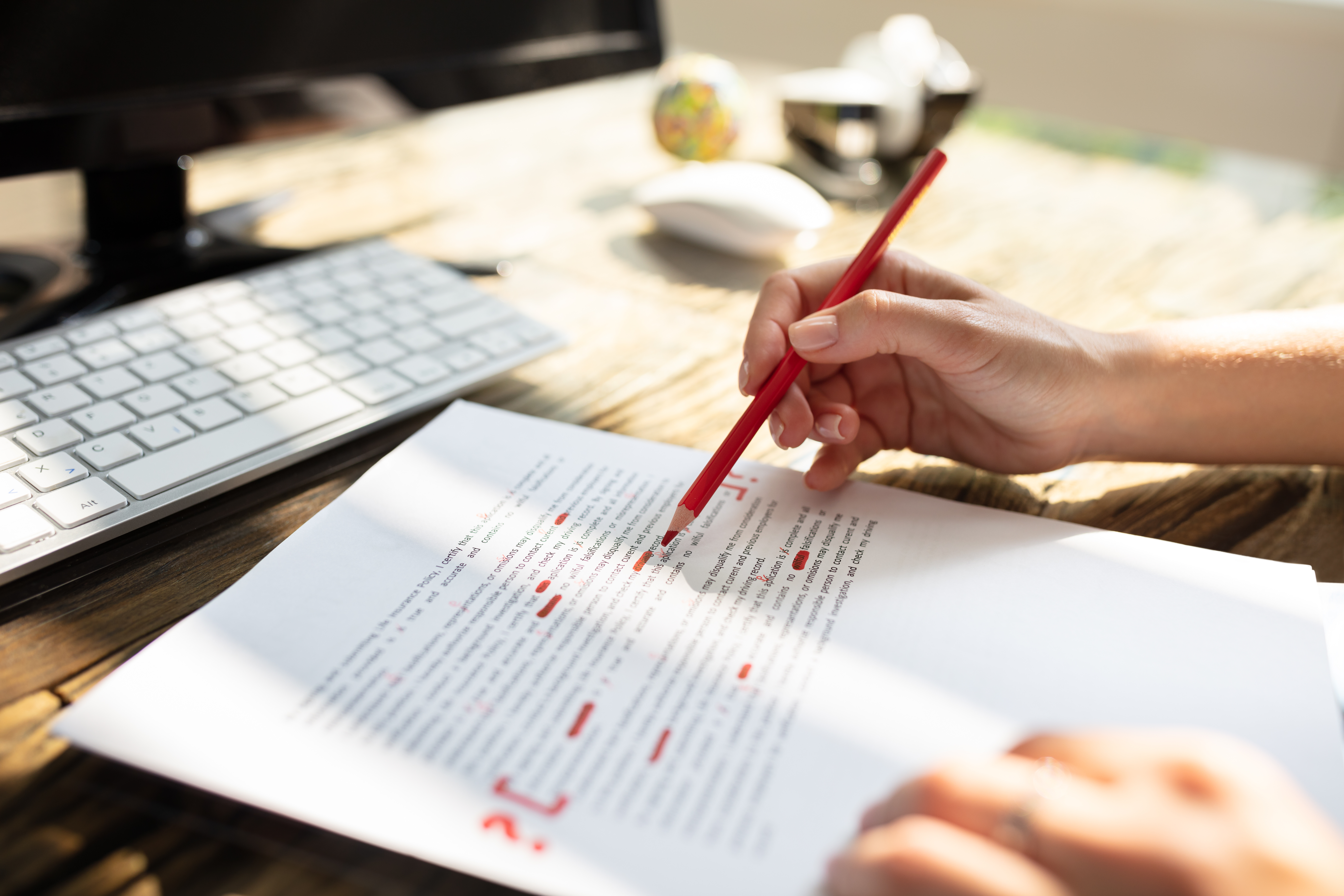 “Author editing a printed manuscript with a red pencil, refining their draft at a wooden desk with a computer nearby.”